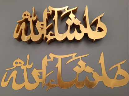 Two Masha Allah-shaped acrylic letters in gold color, displayed against a dark background.